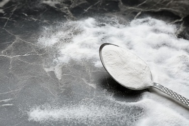 Spoon with baking soda on grey background, closeup. Space for text