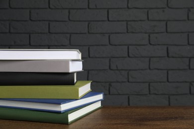 Photo of Stack of hardcover books on wooden table near dark brick wall, space for text