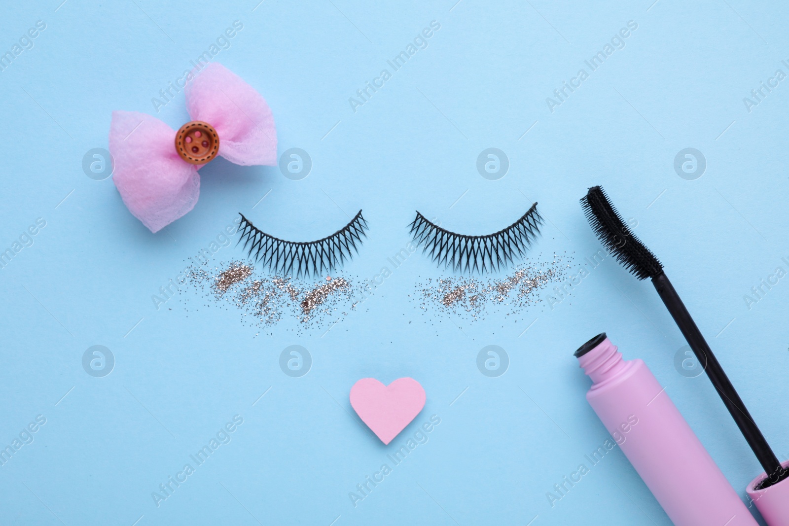 Photo of False eyelashes, heart and glitter as beautiful face on light blue background, flat lay