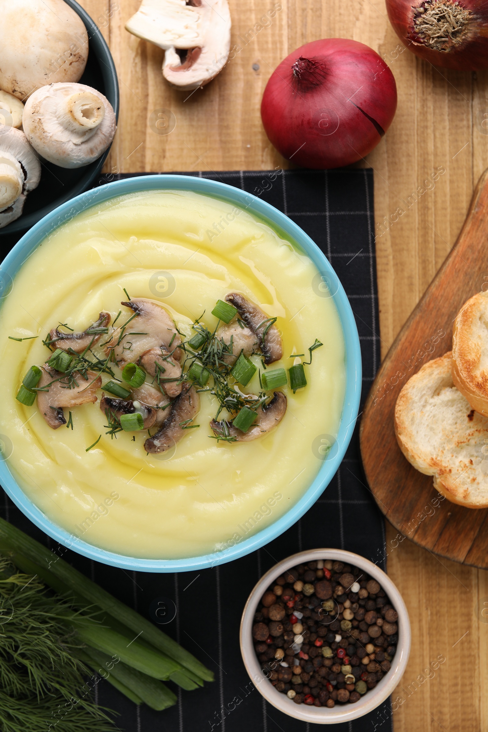 Photo of Bowl of tasty cream soup with mushrooms, green onions and dill on wooden table, flat lay