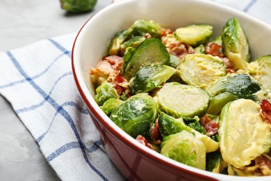 Photo of Delicious Brussels sprouts with bacon in baking pan on grey table, closeup