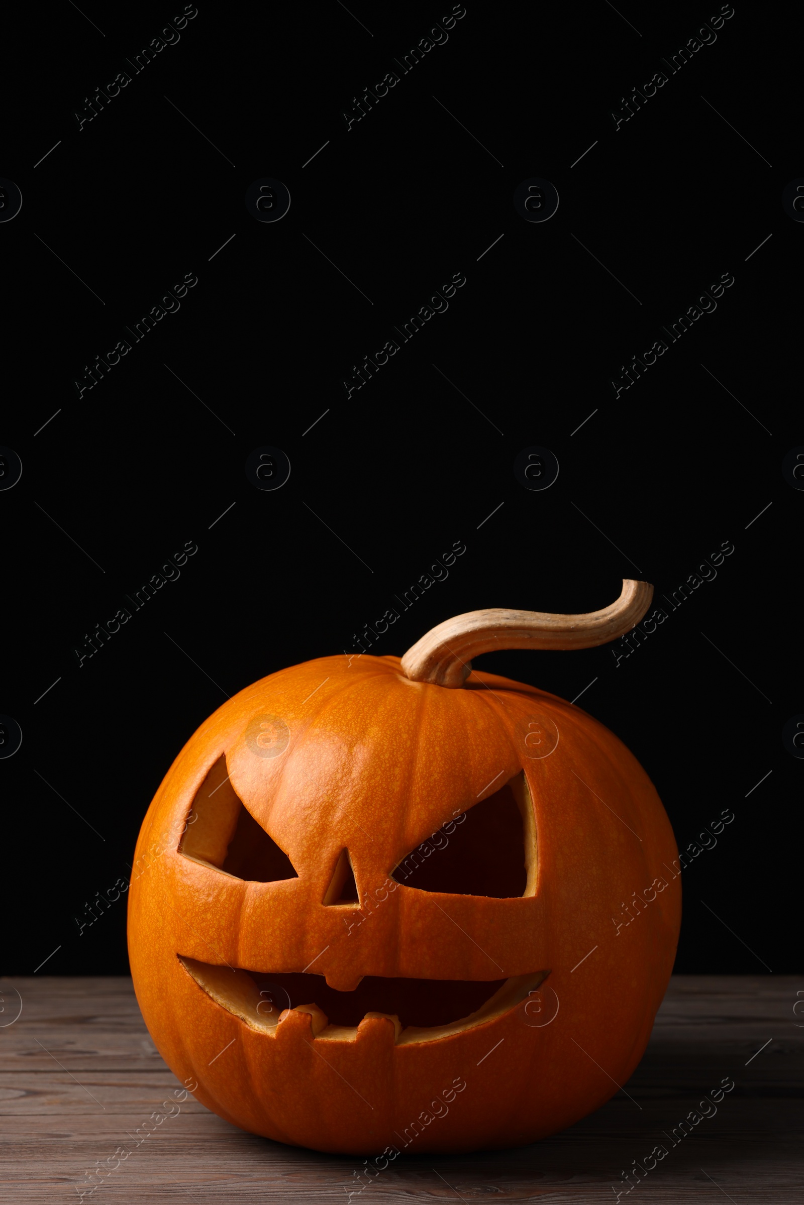 Photo of Scary jack o'lantern made of pumpkin on wooden table against black background, space for text. Halloween traditional decor
