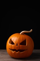 Scary jack o'lantern made of pumpkin on wooden table against black background, space for text. Halloween traditional decor