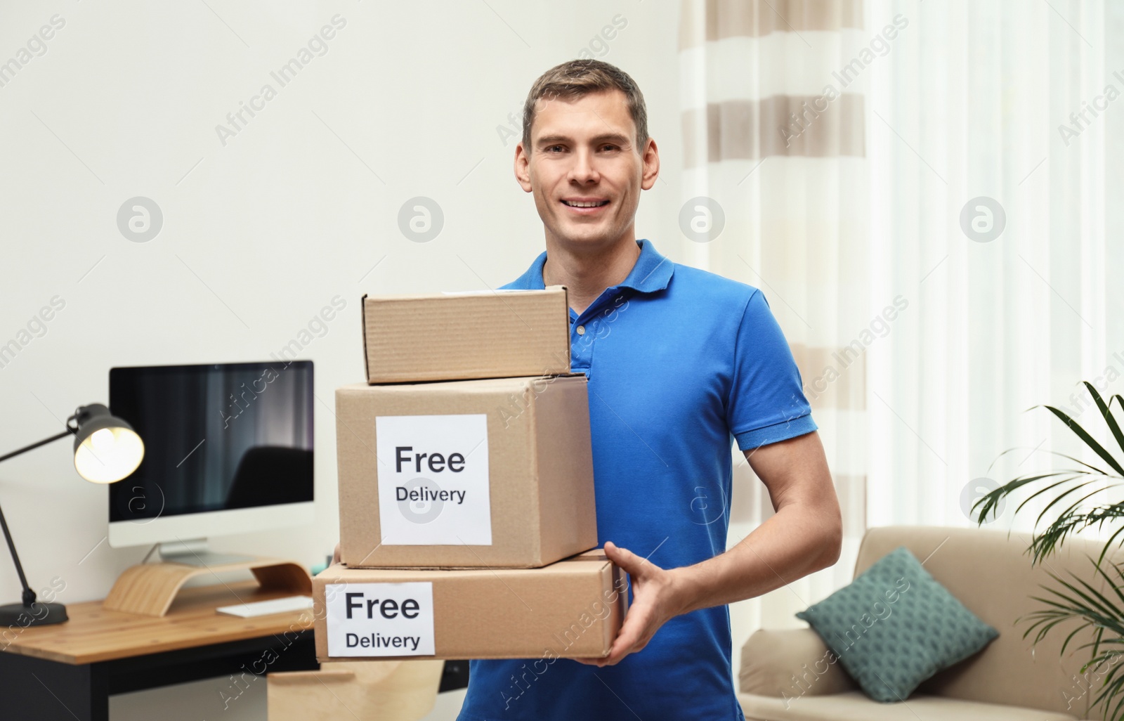 Photo of Courier holding parcels with stickers Free Delivery indoors