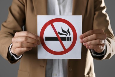 Woman holding card with no smoking sign on gray background, closeup