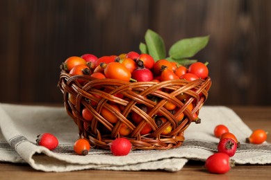 Photo of Ripe rose hip berries with green leaves on wooden table