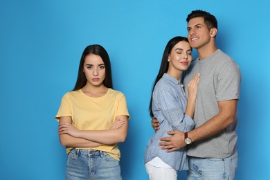 Unhappy woman feeling jealous while couple spending time together on blue background