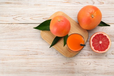 Photo of Tasty grapefruit juice in glass and fresh fruits on light wooden table, flat lay. Space for text