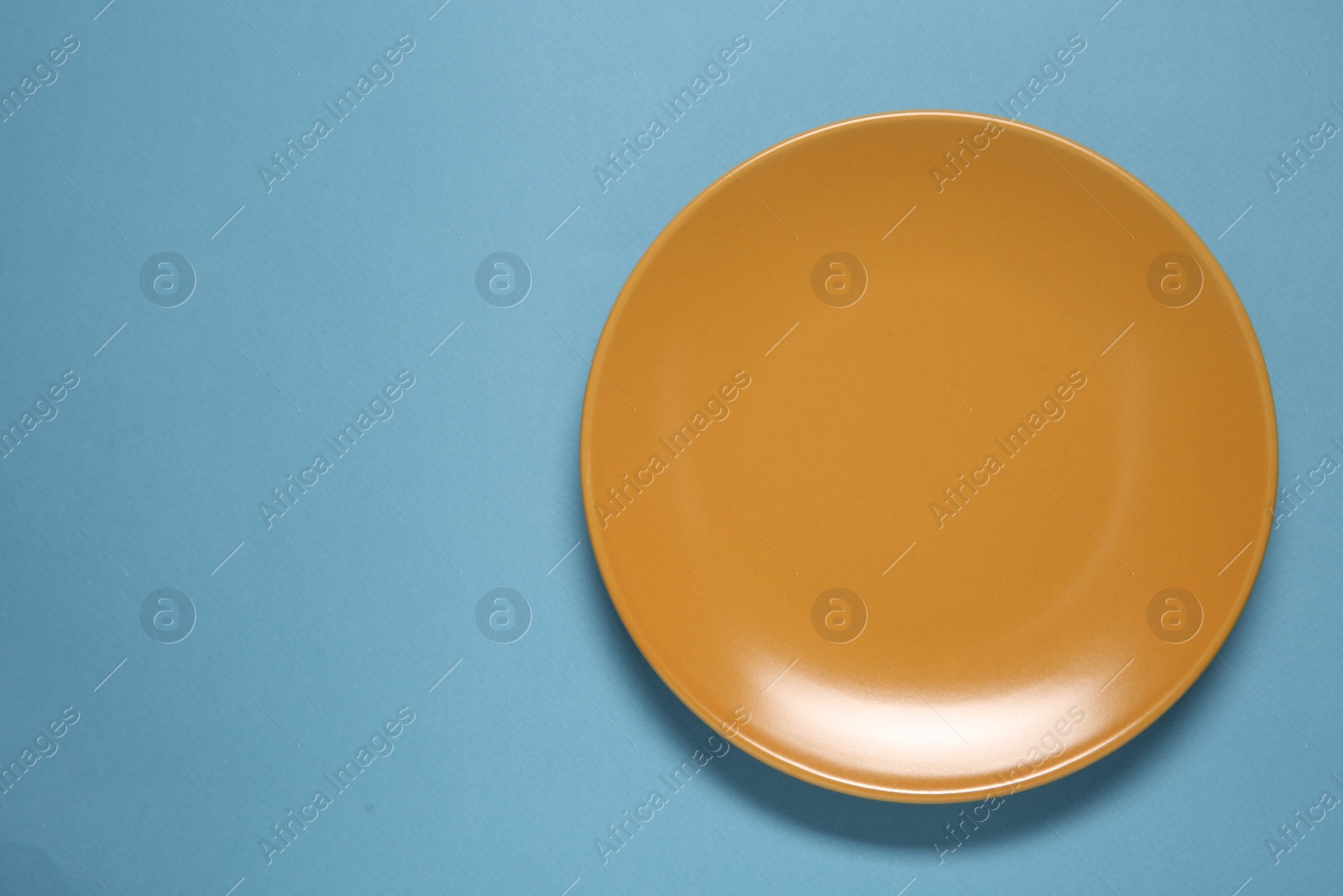 Photo of One orange ceramic plate on light blue background, top view. Space for text