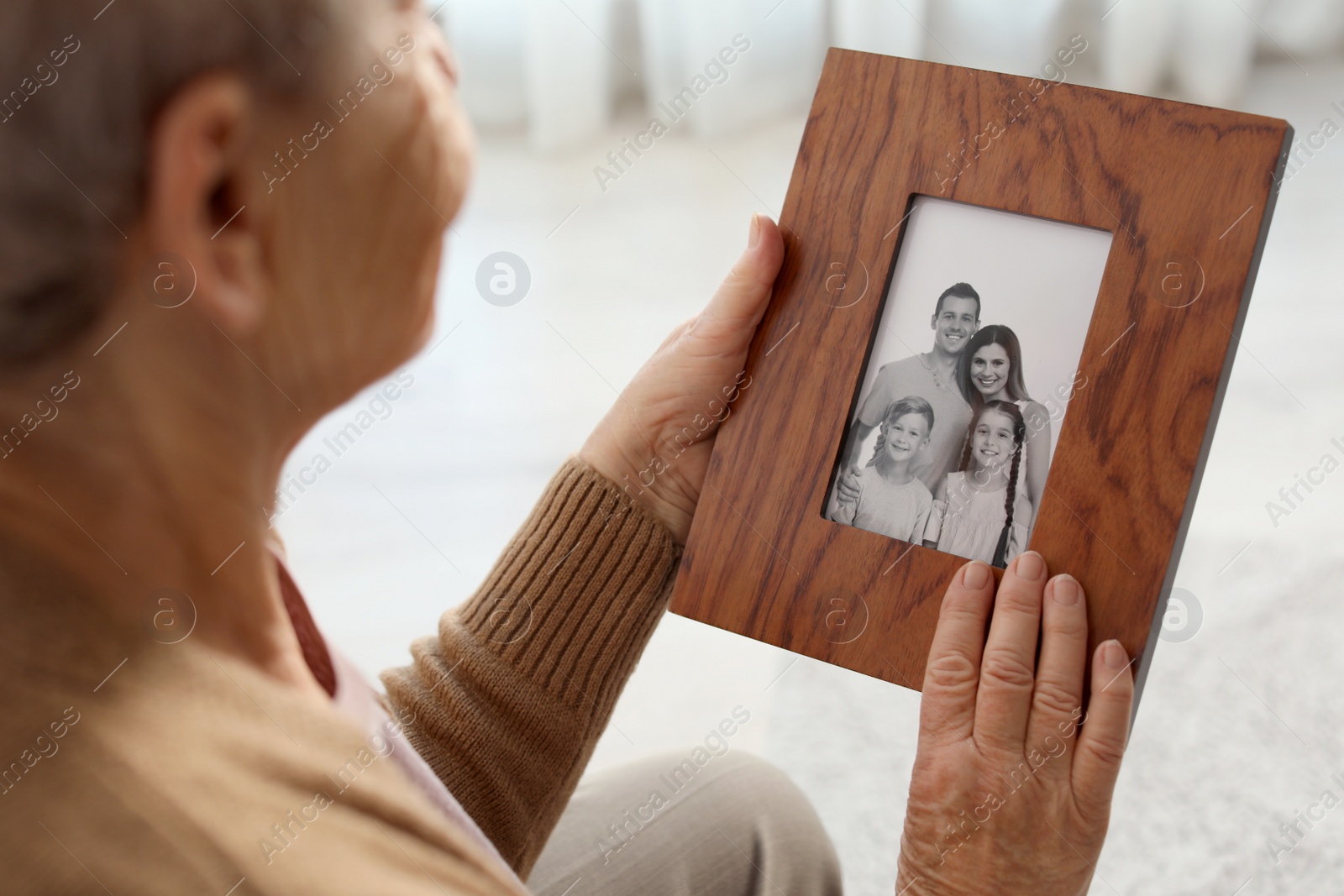 Photo of Elderly woman with framed family portrait at home