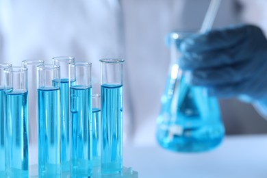 Scientist holding flask near test tubes with light blue liquid, selective focus