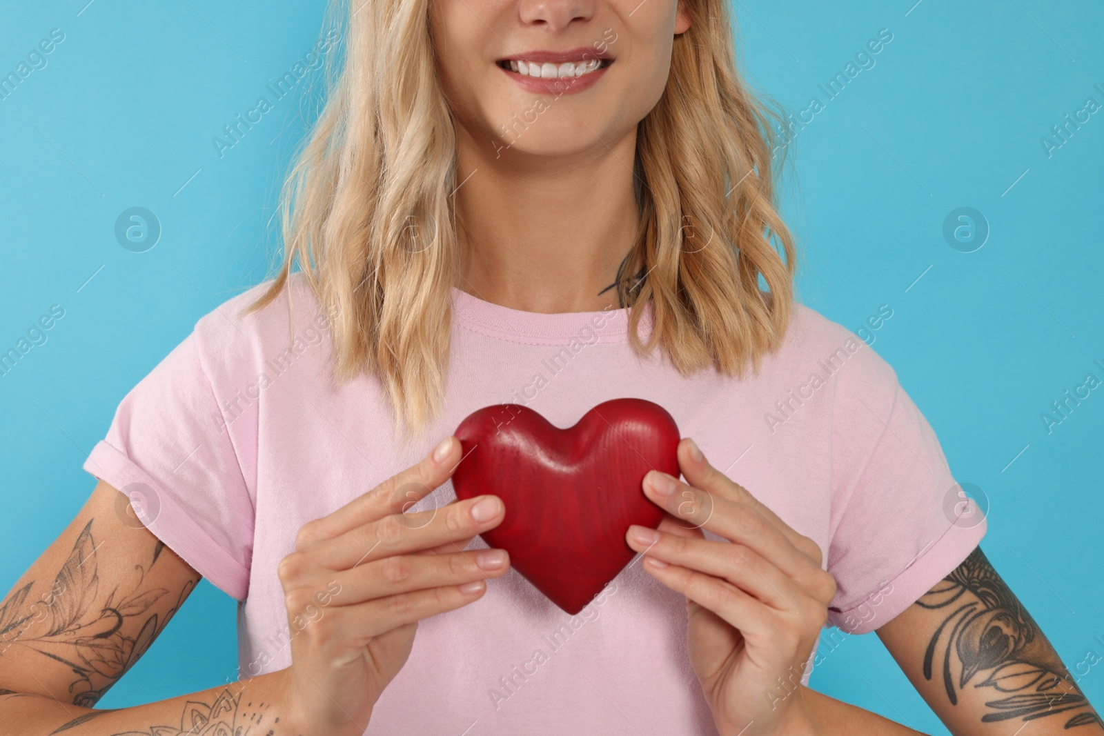 Photo of Happy volunteer holding red heart with hands on light blue background, closeup