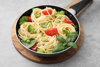 Photo of Delicious pasta primavera in frying pan and ingredients on light gray table, closeup