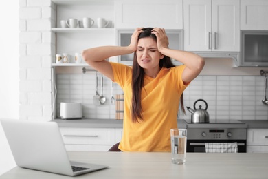 Photo of Young woman suffering from headache in kitchen