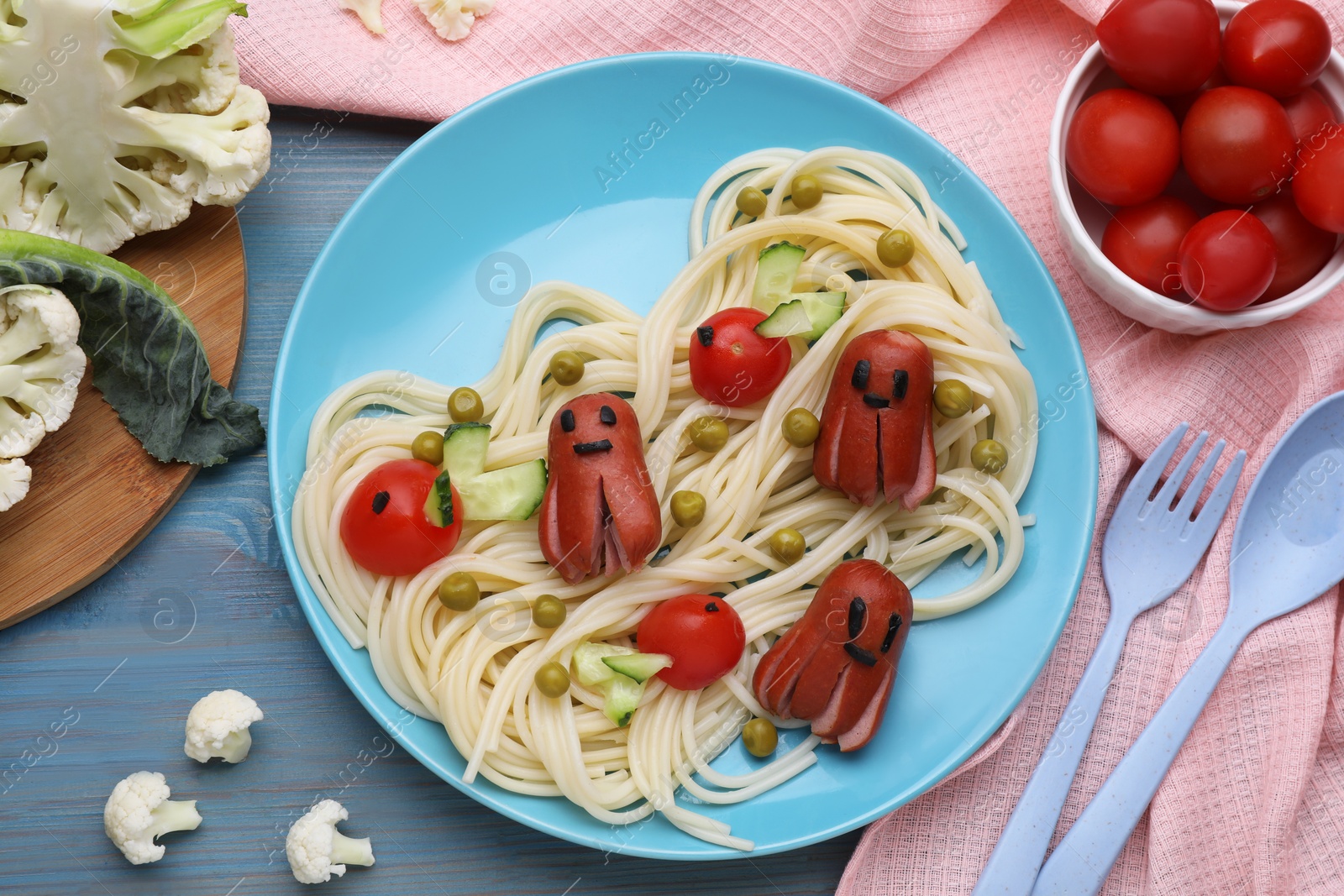 Photo of Creative serving for kids. Plate with cute octopuses made of sausages, pasta and vegetables on light blue wooden table, flat lay