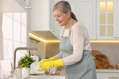 Happy housewife washing plate in kitchen sink