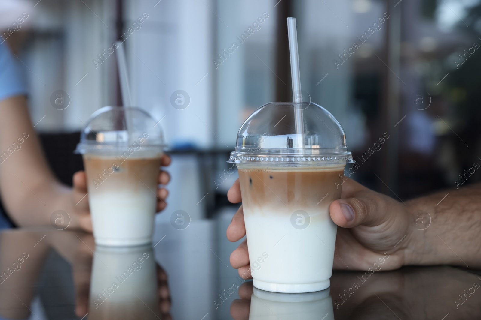 Photo of Man and woman with plastic takeaway cups of delicious iced coffee at table in outdoor cafe, closeup
