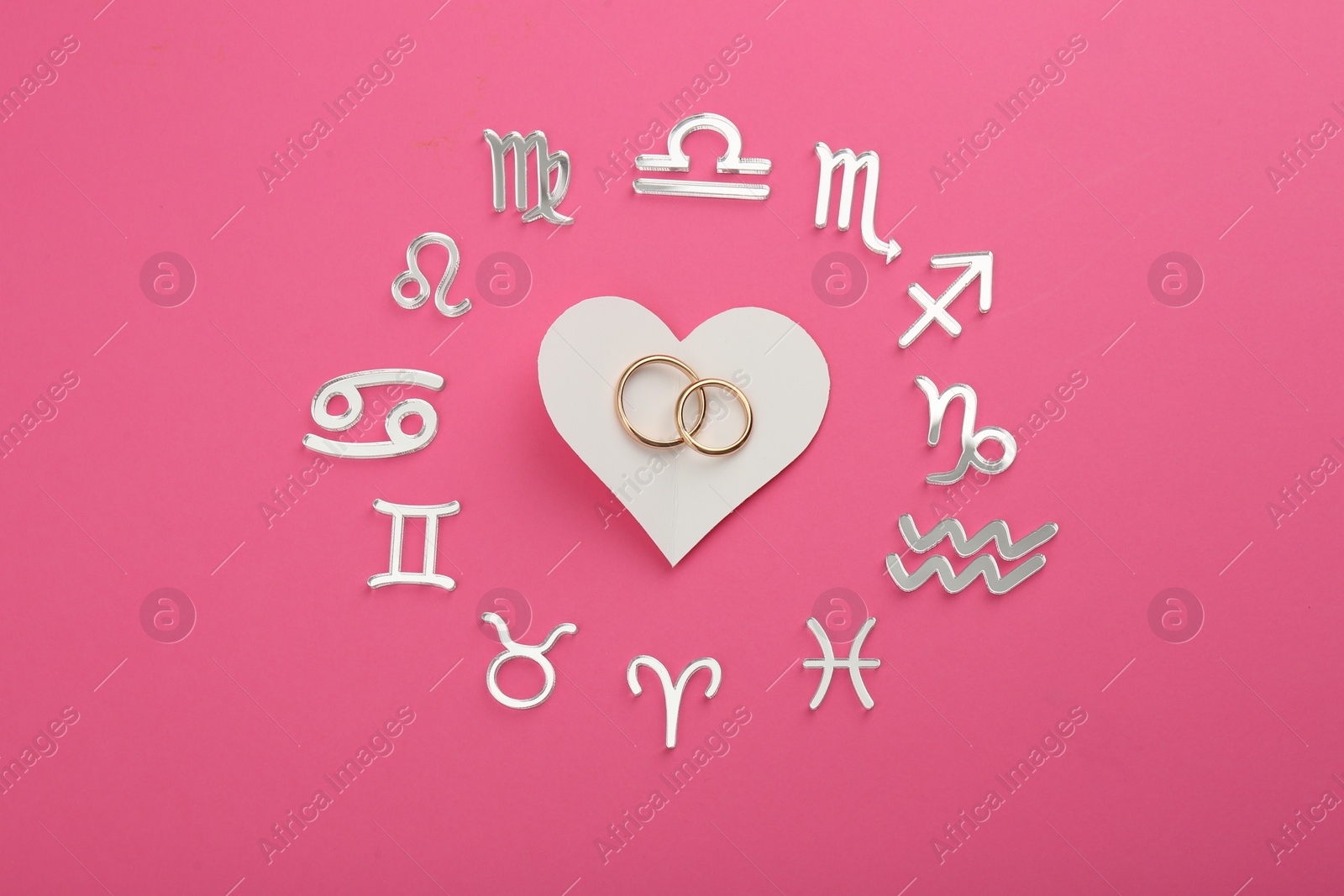 Photo of Zodiac signs, heart and wedding rings on pink background, flat lay
