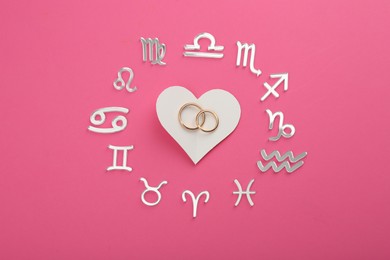 Zodiac signs, heart and wedding rings on pink background, flat lay