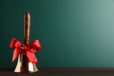 Photo of Golden bell with red bow on wooden table near green chalkboard, space for text. School days