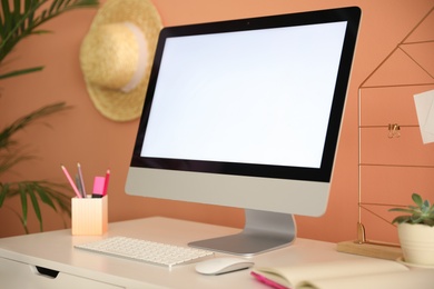 Comfortable workplace with modern computer on table near orange wall. Space for design