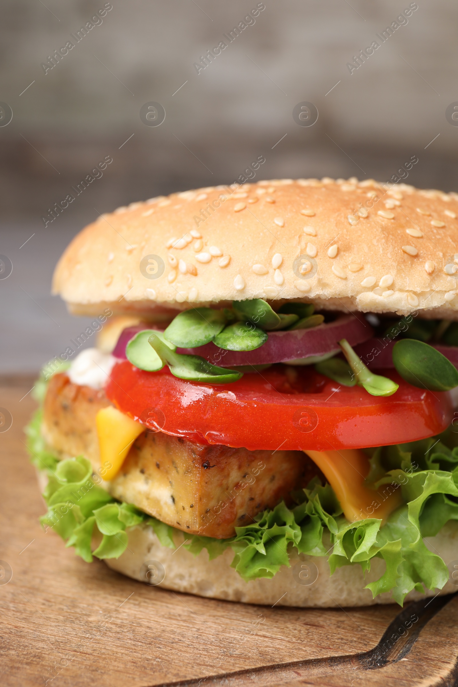 Photo of Delicious burger with tofu and fresh vegetables on wooden board, closeup