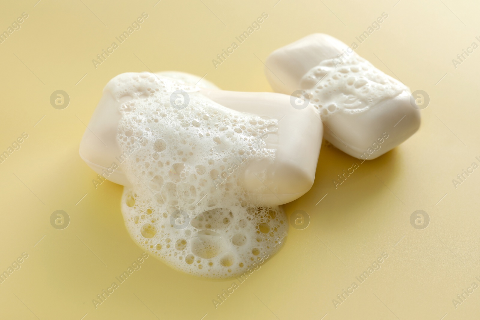Photo of Soap bars with fluffy foam on yellow background