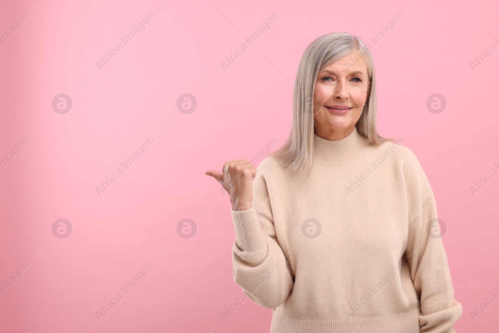 Photo of Portrait of beautiful middle aged woman pointing at something on pink background, space for text