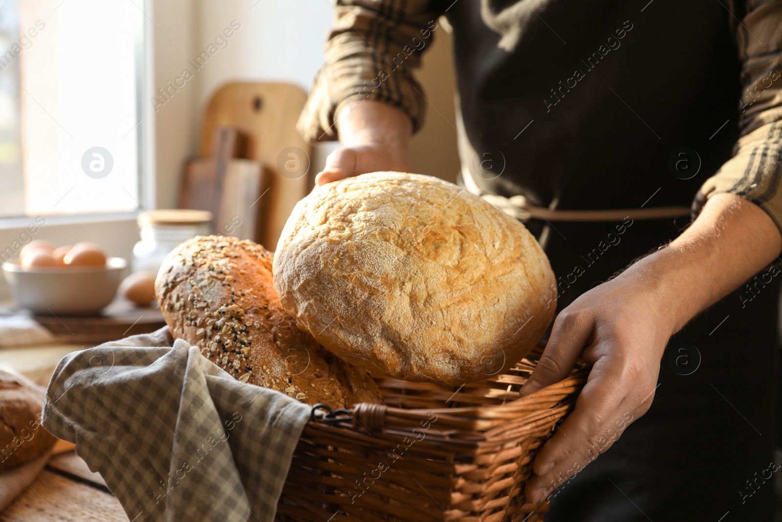 Photo of Man holding wicker basket with different types of bread at table indoors, closeup