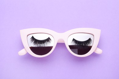 Sunglasses with false eyelashes on violet background, top view
