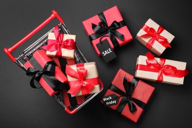 Photo of Cart with gift boxes on dark background, flat lay. Black Friday sale