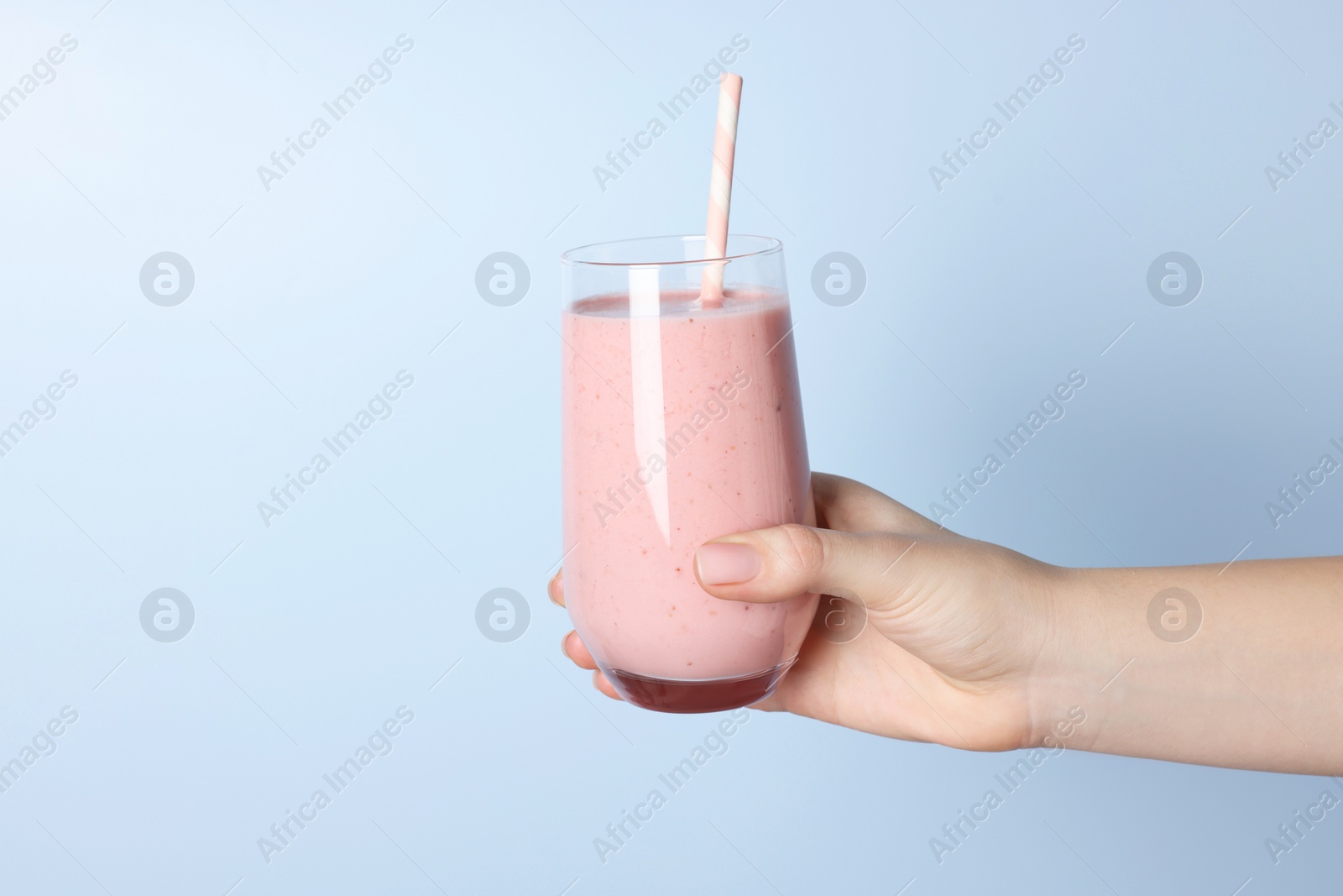 Photo of Woman holding glass of tasty smoothie on light blue background, closeup