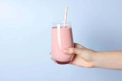 Photo of Woman holding glass of tasty smoothie on light blue background, closeup