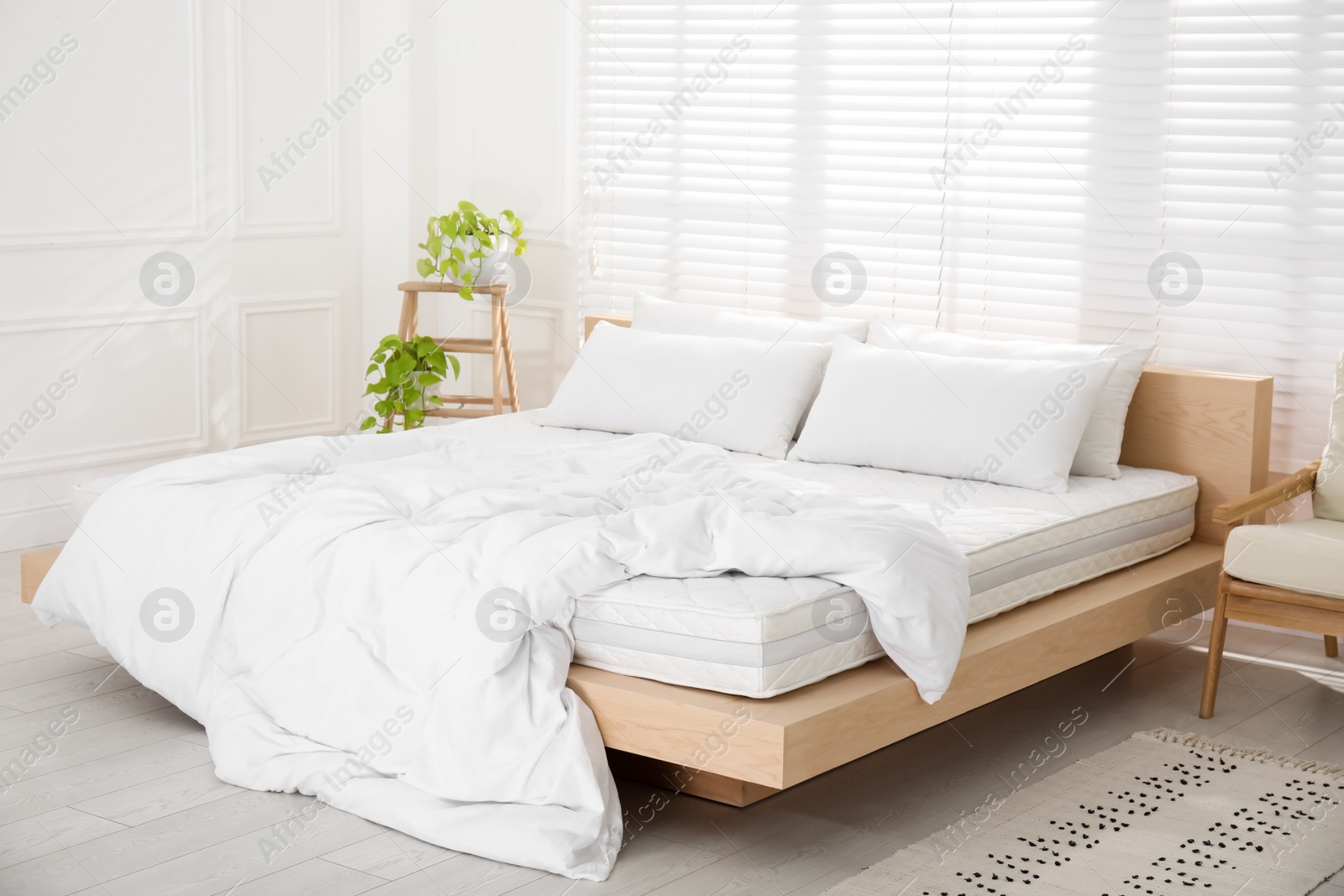 Photo of Wooden bed with soft white mattress, blanket and pillows in cozy room interior