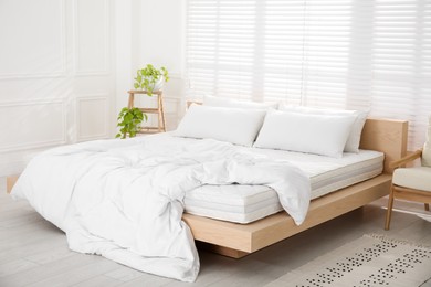 Wooden bed with soft white mattress, blanket and pillows in cozy room interior