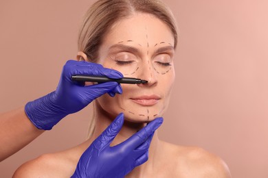 Doctor with marker preparing patient for cosmetic surgery operation on light brown background, closeup