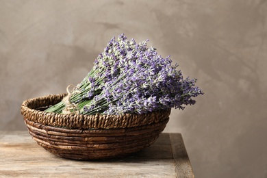 Photo of Fresh lavender flowers in basket on wooden table against beige background, space for text