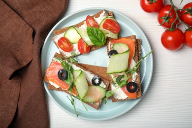 Photo of Tasty rye crispbreads with salmon, cream cheese and vegetables served on white wooden table, flat lay