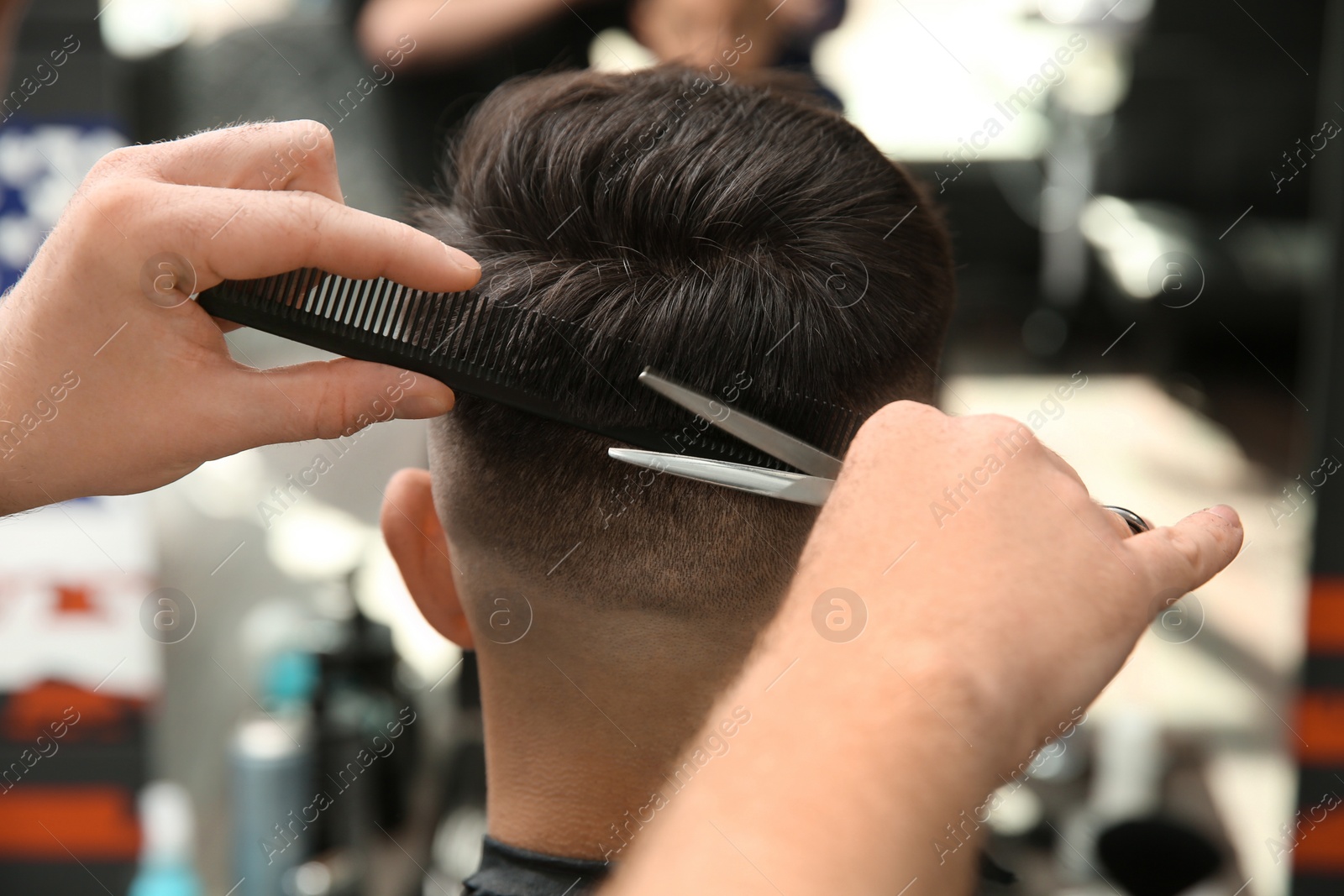 Photo of Professional barber making stylish haircut in salon, closeup