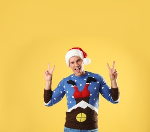 Photo of Portrait of young man in Christmas sweater and Santa hat on yellow background