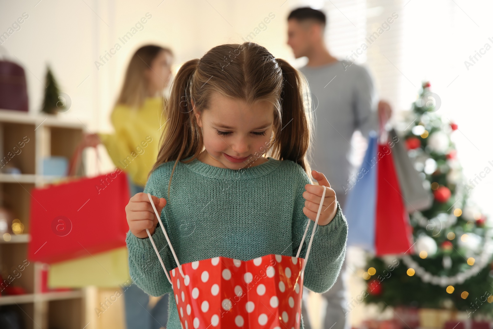 Photo of Little girl with bag near her parents in store. Family Christmas shopping