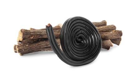 Photo of Tasty black candy and dried sticks of liquorice root on white background
