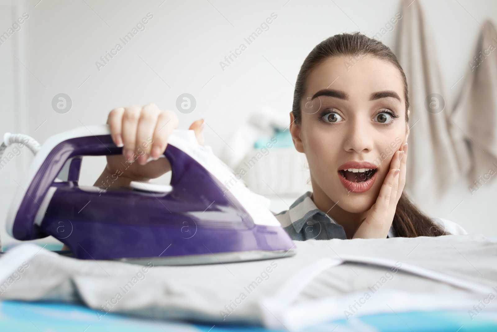 Photo of Young woman ironing clothes at home