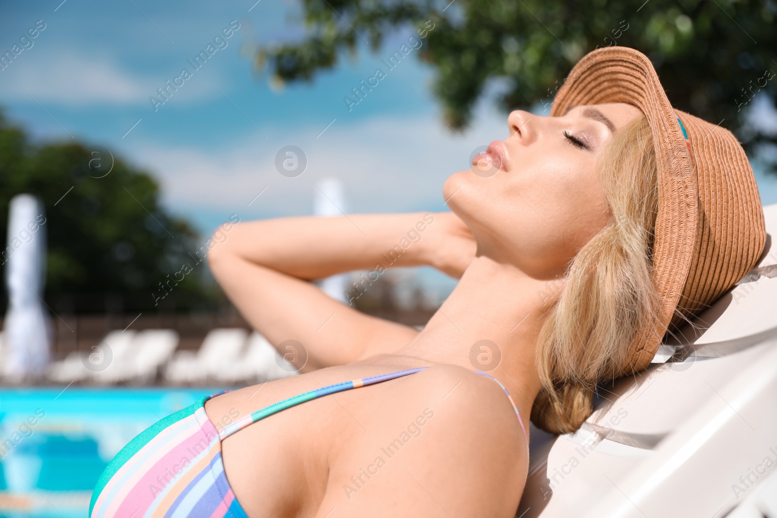 Photo of Sexy young woman in stylish bikini with hat relaxing on sunbed near swimming pool outdoors