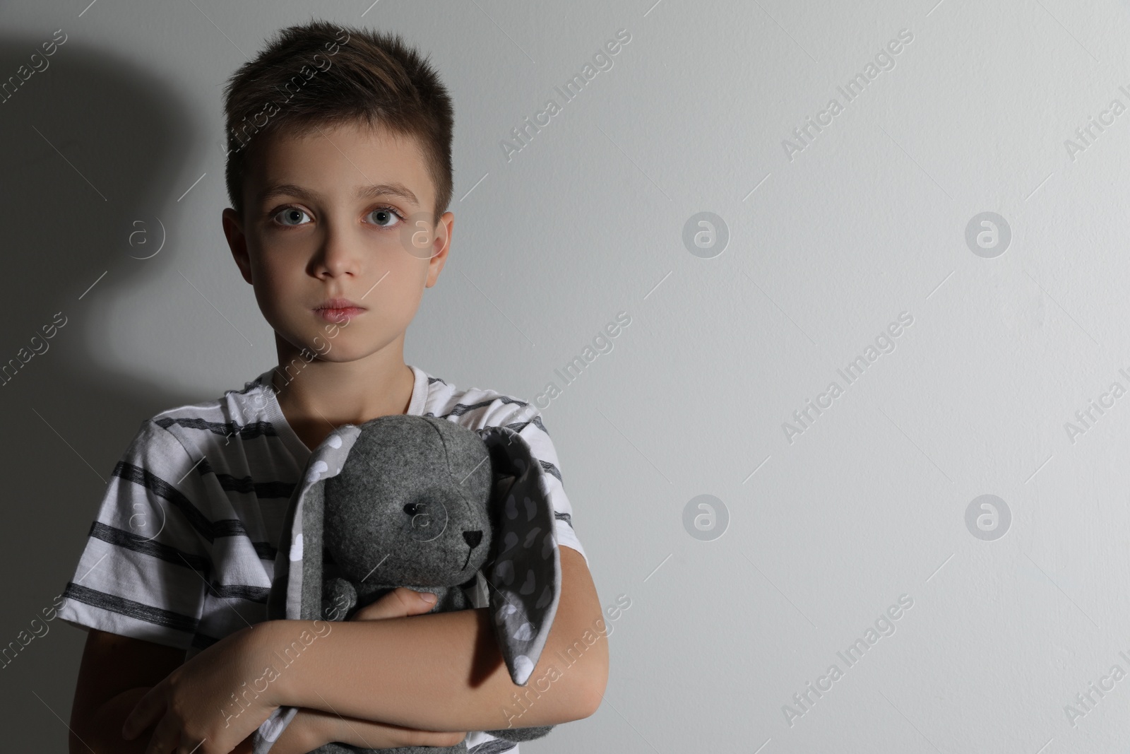 Photo of Sad little boy with toy near white wall, space for text. Domestic violence concept