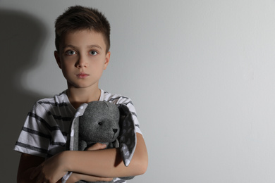Sad little boy with toy near white wall, space for text. Domestic violence concept