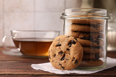 Photo of Glass jar with delicious chocolate chip cookies and tea on wooden table, closeup. Space for text