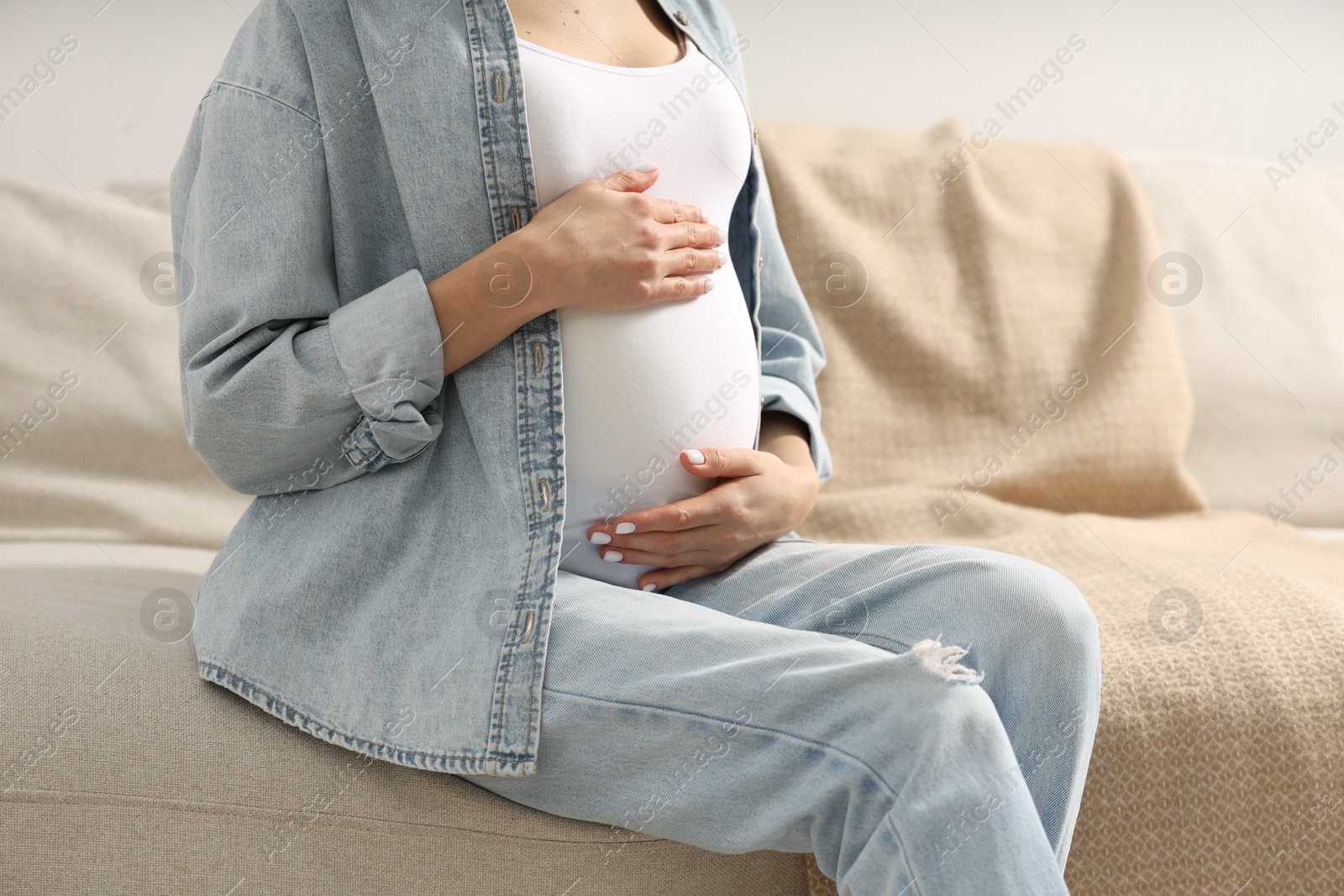 Photo of Pregnant woman touching her belly on sofa at home, closeup