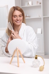 Beautiful woman brushing her hair at vanity in room