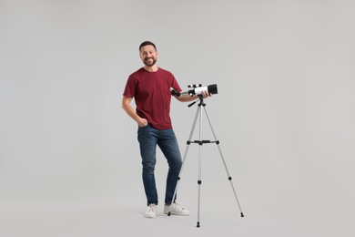 Happy astronomer with telescope on light grey background